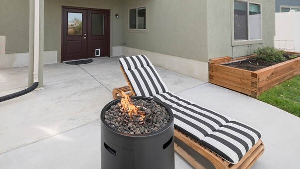 A concrete patio with a fire pit and lounge chair with a wooden planter box