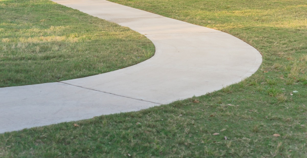 A level concrete sidewalk going through open grass